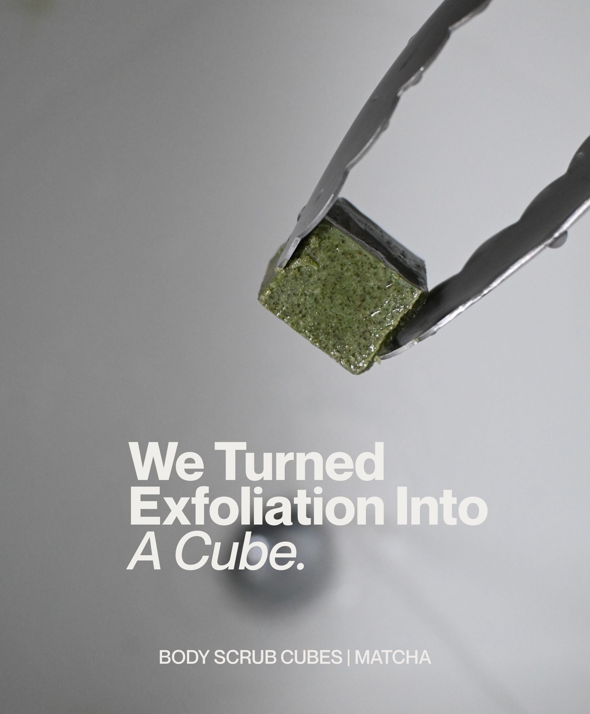Matcha body scrub cube held with metal tongs in minimalist bathroom setting